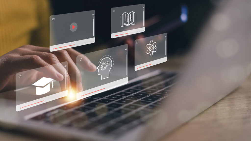 Hands over a laptop keyboard with floating e-learning icons: graduation cap, atom symbol, user profile with gears, and video player overlay.