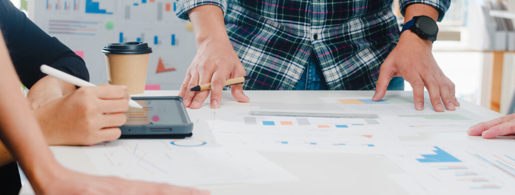 Hands of people over a tablet and papers with charts on a desk during a brainstorming session on gamification strategy.