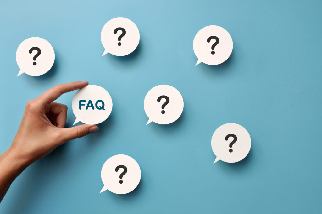 Hand holding a speech bubble labeled “FAQ” surrounded by question mark icons on a blue background, representing frequently asked questions.