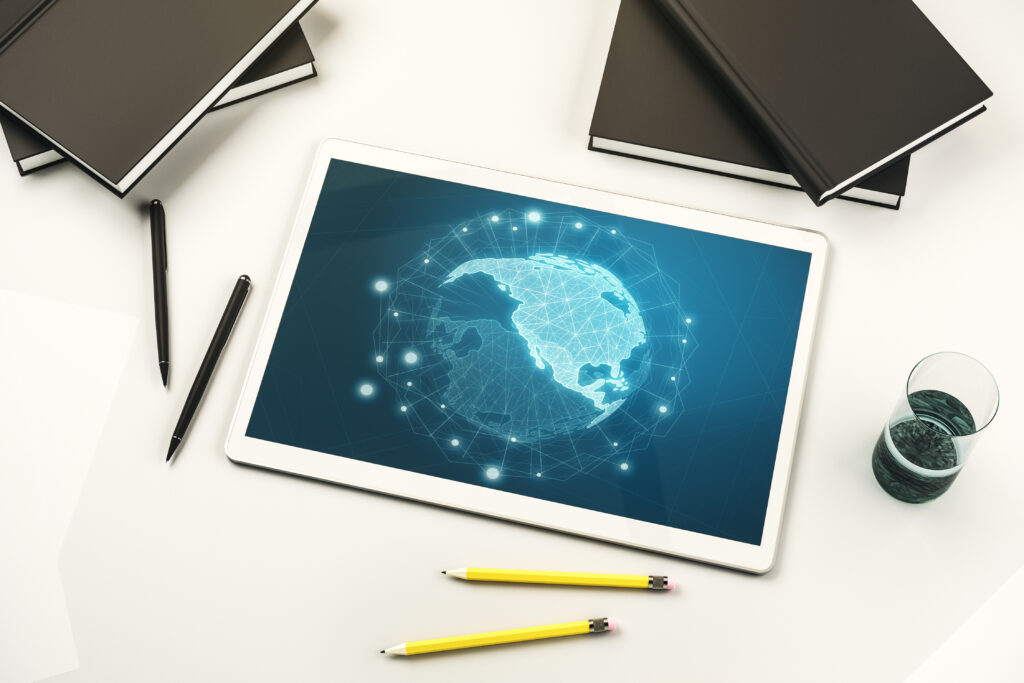 Tablet on a desk displaying a digital world map with network connections, surrounded by notebooks, pens, pencils, and a glass of water.
