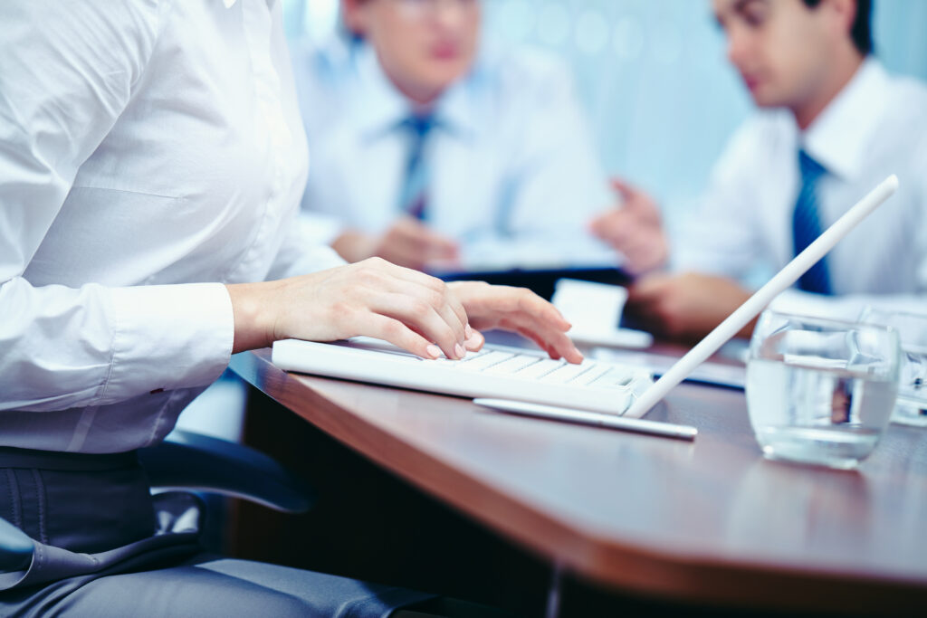 Hands of businesswoman typing on laptop with her colleagues on background
